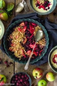 Juicy ripe burst berries covered with a layer of crunchy toasted millet and golden flaky oats; vegan gluten-free Apple and Blackberry Crumble recipe. Edward Daniel ©.